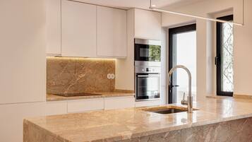 A modern kitchen with white cabinetry, a marble countertop, and stainless steel appliances.