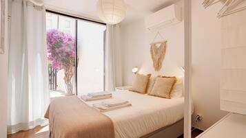 Slaapkamer met een bed, gordijnen, een macramé wanddecoratie en een raam met uitzicht op roze bloemen.