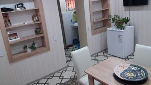 Un comedor con una mesa y sillas de madera, un refrigerador blanco y estantes de madera con diversos objetos.