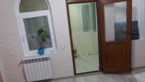 Una habitación con una cama, un radiador, una ventana con una planta y una puerta.