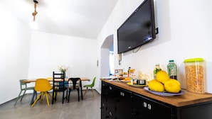A modern kitchen with a flat-screen TV mounted on the wall, a wooden countertop with various food items, and a dining area with chairs and a table. - Monca's House (Vietri sul Mare)