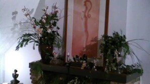 A fireplace with a brick surround and a mantel decorated with plants and a framed picture.