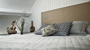 A modern bedroom with a sloped ceiling, a bed with patterned pillows, decorative statues, and a small plant.