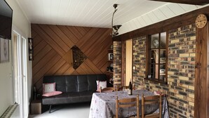 A cozy dining area with a wooden table set for two, a black sofa, and a brick wall with a clock. - Gîte du ROCHER, 3 * in Alsace center (Lapoutroie)