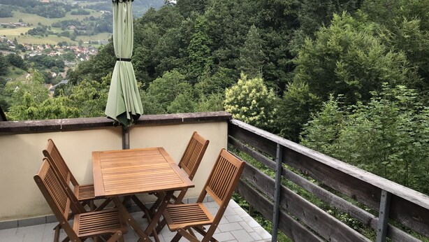 A terrace with a wooden table and chairs, an umbrella, and a view of a forested valley. - Gîte du ROCHER, 3 * in Alsace center (Lapoutroie)