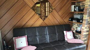 A black leather sofa with two red and white checkered pillows, a wooden wall with a diamond pattern, and a brick wall with shelves holding books and speakers. - Gîte du ROCHER, 3 * in Alsace center (Lapoutroie)