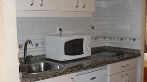 Eine Küche mit weißen Schränken, einer Granit-Arbeitsplatte, einer weißen Mikrowelle und einem Edelstahl-Spülbecken.