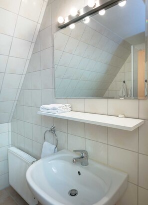 Une salle de bain avec un lavabo blanc, un miroir avec éclairage intégré, un porte-serviettes et une étagère.