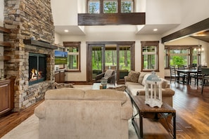 A spacious living room with a stone fireplace, large windows, and a high ceiling. - Great VALUE on the 17th Tee! Sunnyside Lodge | Hot Tub | Game Room (Cle Elum)