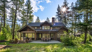 A two-story house with a stone chimney, large windows, and a patio with outdoor furniture.