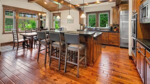 A spacious kitchen with wooden cabinets, a large island with bar stools, and a view of the outdoors through large windows.