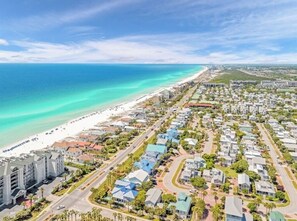 An aerial view of a coastal residential area with a beach, houses, and a large hotel complex.