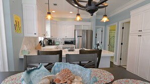 A modern kitchen with white cabinets, stainless steel appliances, and a dining area with a table set for two. - STEPS TO CRYSTAL BEACH see picture for location (Destin)