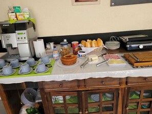 Een ontbijtbuffet met een koffieapparaat, diverse etenswaren en bestek op een tafel.