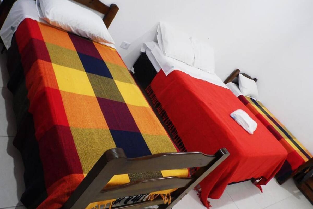 Une chambre avec deux lits, l’un recouvert d’une couverture à carreaux colorés et l’autre d’une couverture rouge.