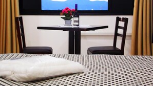 Ein Hotelzimmer mit Bett, Tisch mit Stühlen, einer Topfpflanze und Blick auf Berge durch ein Fenster.