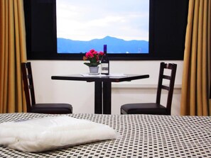 Ein Hotelzimmer mit Bett, Tisch mit Stühlen, einer Topfpflanze und Blick auf Berge durch ein Fenster.