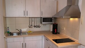 Eine kleine Küchenzeile mit Spüle, Mikrowelle, Kaffeemaschine und hängenden Küchenutensilien.