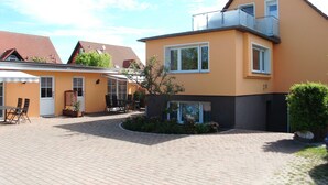 Ein zweistöckiges Haus mit Balkon, einer Terrasse und Gartenmöbeln sowie einer gepflasterten Auffahrt.