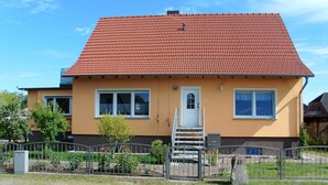 Ein zweistöckiges Haus mit rotem Ziegeldach, einer Haustür und einer kleinen Treppe zum Eingang.