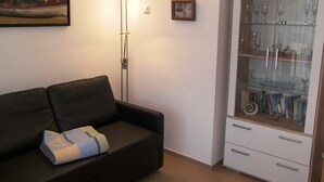 Ein Wohnzimmer mit einer schwarzen Couch, einer Glasvitrine mit Weingläsern und einem Gemälde an der Wand.