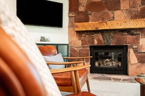 A living room with a stone fireplace, a mounted television, and a leather armchair.