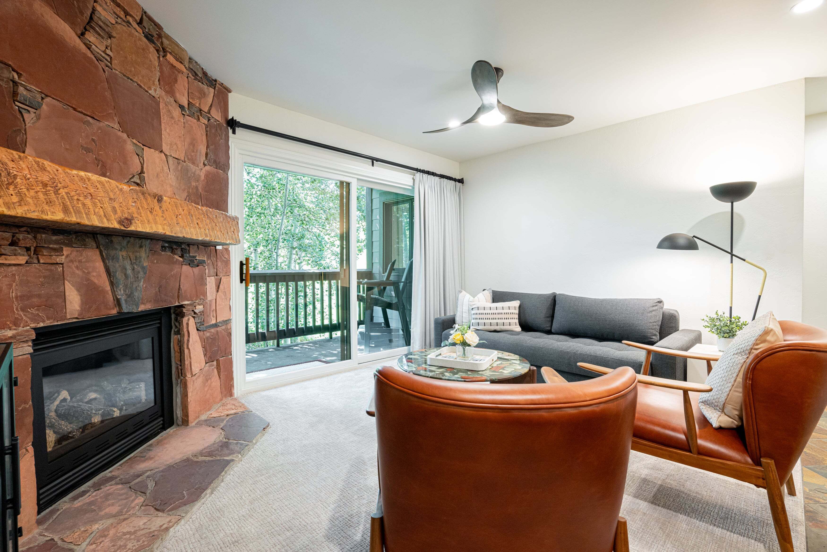A living room with a stone fireplace, a sofa, leather chairs, a coffee table, and a ceiling fan.