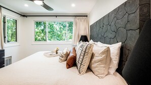 Una camera da letto con un letto grande, un ventilatore a soffitto, una finestra con tende e una parete dall'aspetto in legno.