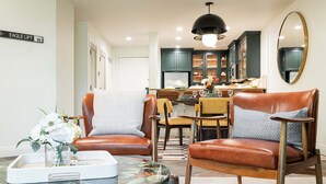 Un soggiorno moderno con poltrone in pelle, un tavolino da caffè in vetro e un'area pranzo illuminata da un lampadario.