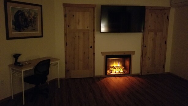 A room with a fireplace, a TV mounted above it, and a desk with a chair. - Fort Wrangell, Orca Room (Wrangell)