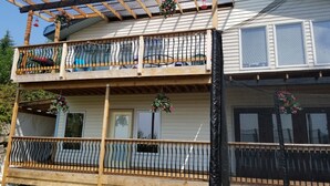 A two-story building with a balcony on the upper floor, a covered area with a wooden roof, and a fenced balcony on the lower floor. - Fort Wrangell, Orca Room (Wrangell)