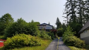 A gravel driveway leading to a house surrounded by dense greenery and trees. - Fort Wrangell, Orca Room (Wrangell)