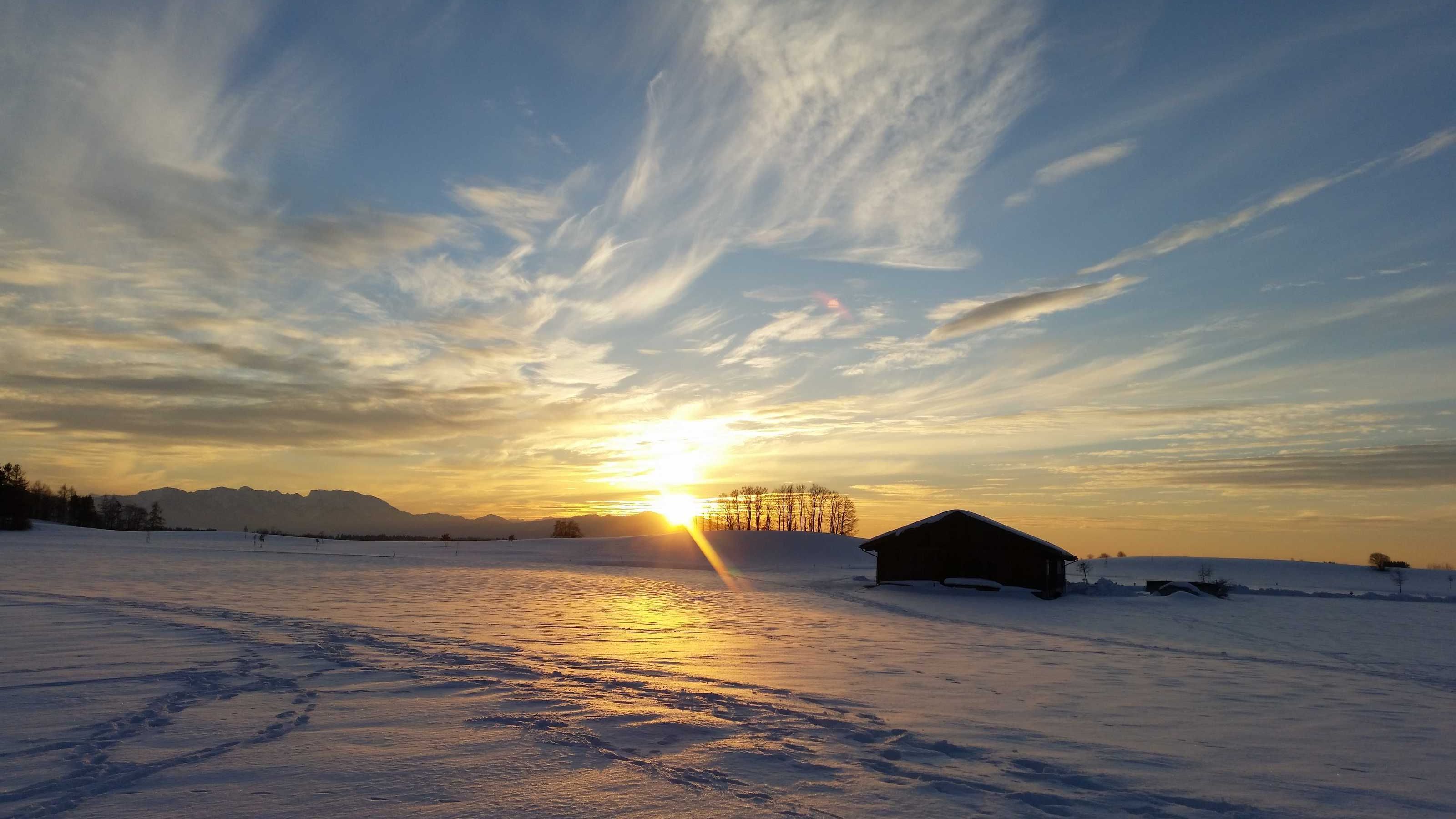 Eine verschneite Landschaft mit einem Gebäude und Bergen im Hintergrund.