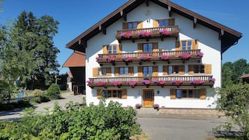 Ein mehrgeschossiges Gebäude mit Balkonen, die mit Blumen geschmückt sind, ein traditionelles Satteldach und ein klarer Himmel.