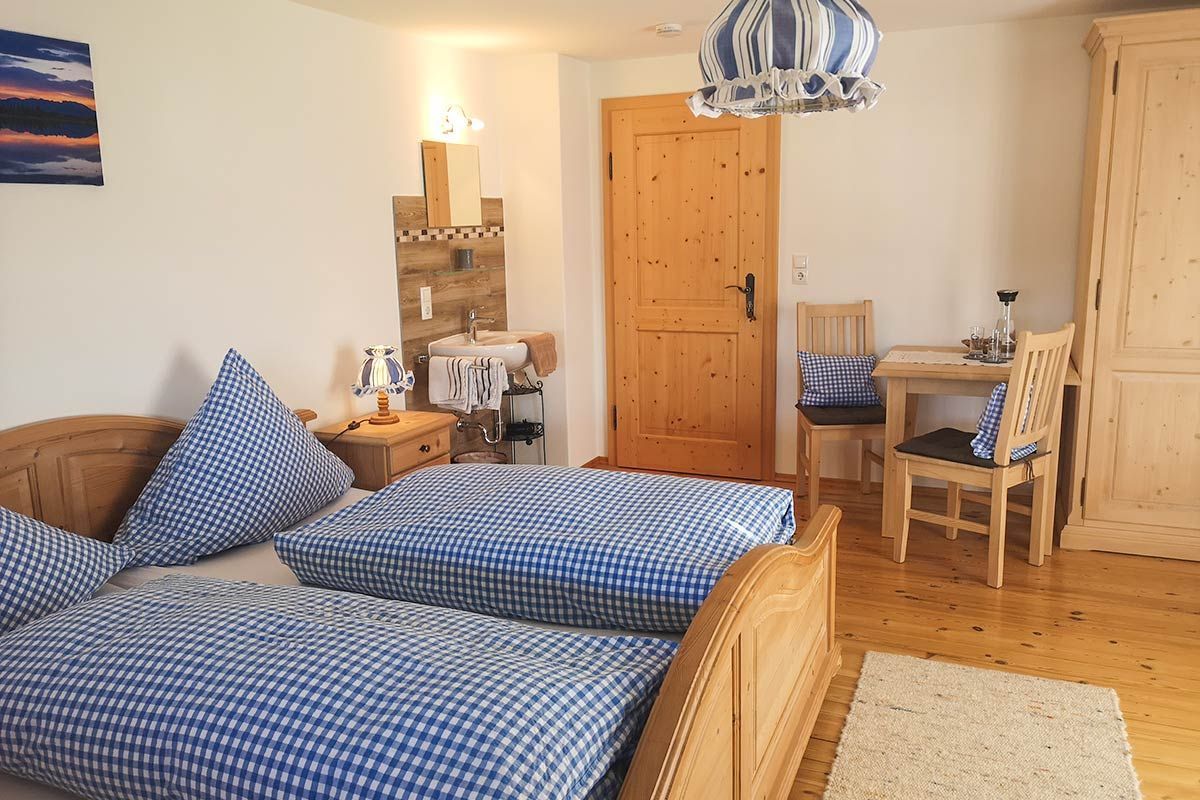 Une chambre à coucher avec un lit en bois, un bureau, une chaise, une armoire en bois et une salle de bain avec un miroir et un lavabo.