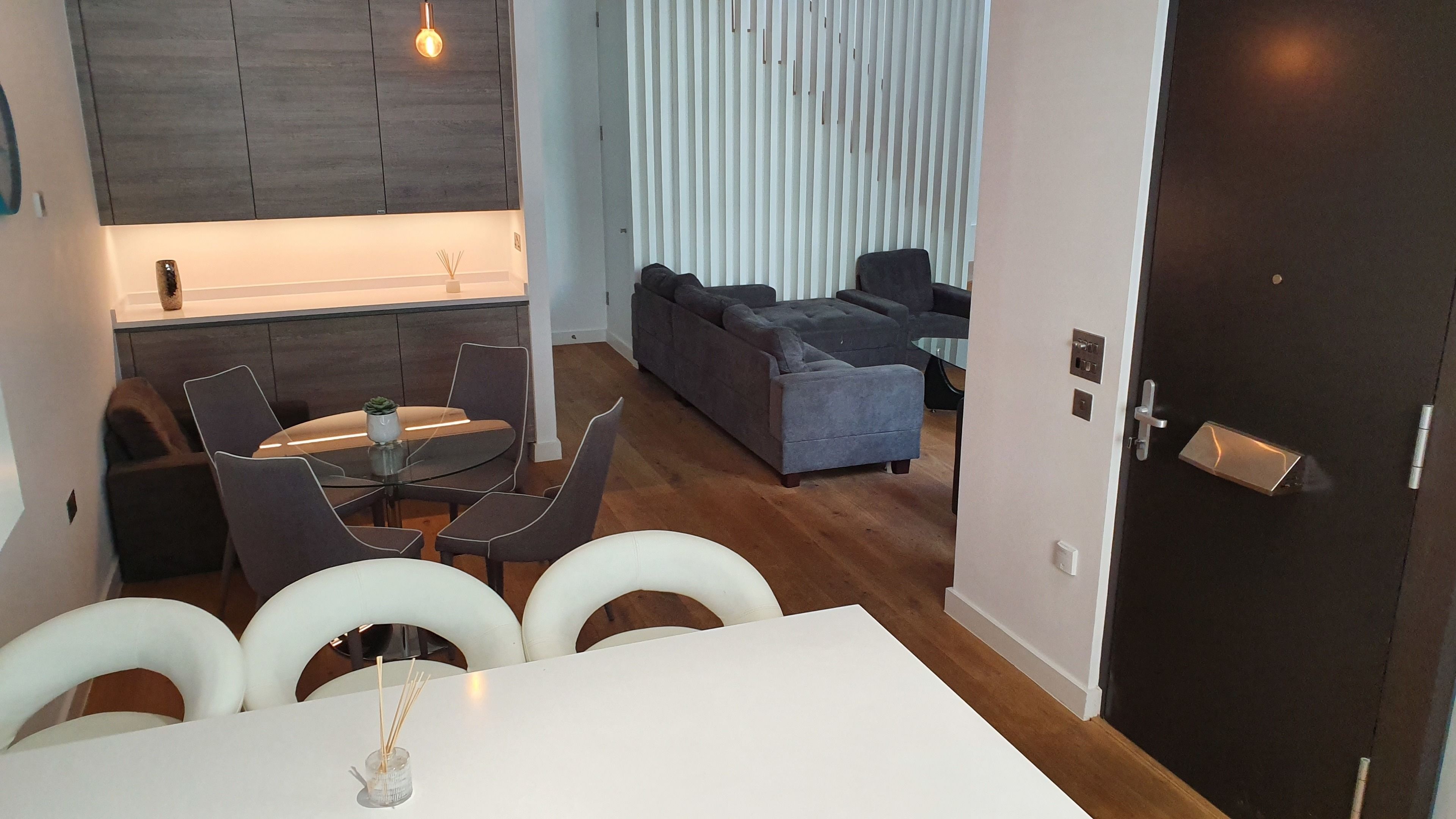 A modern living room with a grey sofa, a glass coffee table, and a dining area with a white table and grey chairs.