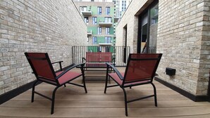 A balcony with two chairs and a table, brick walls, and a view of multi-story buildings.