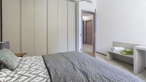 Un dormitorio con cama, mesita de noche, lámpara, armario y baño visible a través de una puerta abierta.