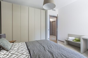 Un dormitorio con cama, mesita de noche, lámpara, armario y baño visible a través de una puerta abierta.