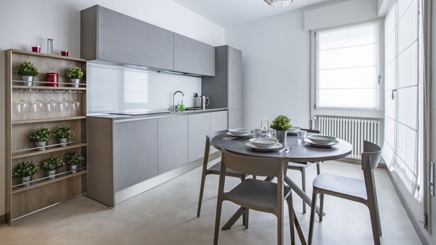 Una cocina moderna con armarios grises, una mesa de comedor con sillas y un ventanal con persianas.
