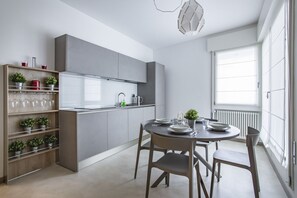 A modern kitchen with grey cabinets, a dining table with chairs, and a window with blinds.