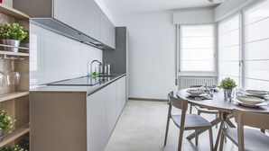 Una cocina moderna con armarios blancos, una campana extractora de acero inoxidable y una zona de comedor con una mesa redonda y sillas.