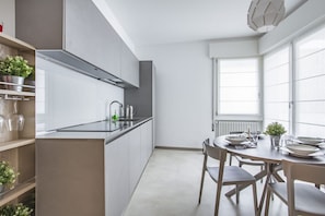 A modern kitchen with white cabinets, a stainless steel range hood, and a dining area with a round table and chairs.