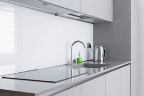 A modern kitchen with a stainless steel sink, a kettle, and a soap dispenser.