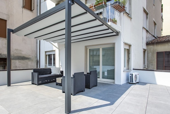 An outdoor patio with a covered seating area, a sliding glass door, and an air conditioning unit.