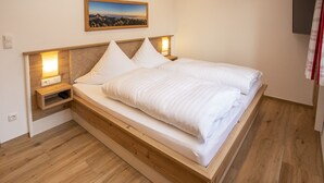 A bed with a wooden frame, white bedding, and a nightstand with a lamp. - (4) Ferienwohnung für 1-4 Personen (63 qm, OG) (Bernau am Chiemsee)