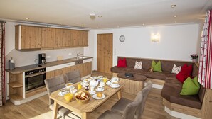 A modern kitchen with wooden cabinets, a dining table set for breakfast, and a cozy seating area with cushions. - (4) Ferienwohnung für 1-4 Personen (63 qm, OG) (Bernau am Chiemsee)