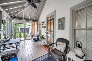 A covered porch with a ceiling fan, a table with chairs, and a wicker chair with a cushion.
