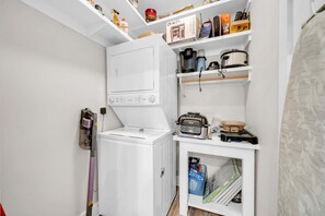 A compact laundry room with a washing machine, a dryer, and a shelf with cleaning supplies. - 2 Complimentary Beach Bikes!  Flirty Flamingo - Pet Friendly, Pool & Beach Access! (Seacrest)