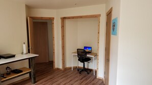 Een kamer met een houten bureau, een stoel en een laptop. Er is een deur die leidt naar een andere kamer en een plank met een koffiezetapparaat.